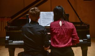 Young artists reading sheet music off of piano bench